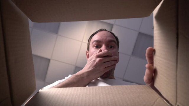 Portrait of happy Caucasian man opening carton box smiling looking at camera expressing positive emotions receiving present. Youth and happiness concept.
