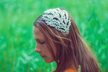 Serious thoughtful young woman wearing a decorative floral headband is looking aside. Profile of a beautiful Russian girl. over a green grass background.