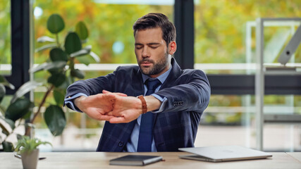 tired businessman with closed eyes and clenched hands near laptop on desk