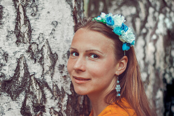 Smiling young woman wearing a decorative floral headband is looking at camera. Close-up portrait of a natural girl without makeup over a birch bark background. Spring is coming.