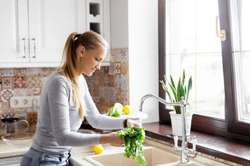 A young woman washes a salad in the sink in the home kitchen. The concept of health and a healthy...