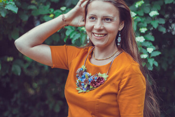 Young woman in an orange dress is looking away. Close-up portrait of a natural girl without makeup with tilted the head over a green background. Spring is coming.