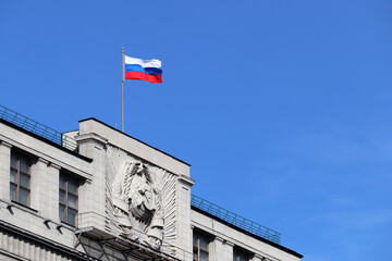 Russian flag on the Parliament building in Moscow on blue sky background. Facade of State Duma of Russia with soviet coat of arms, russian authority