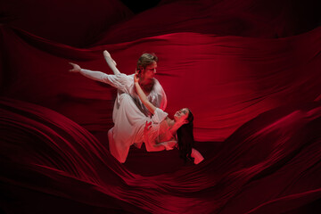 Fondly. Young and graceful ballet dancers on red cloth background in classic action. Art, motion, action, flexibility, inspiration concept. Flexible caucasian couple with billowing red waves.