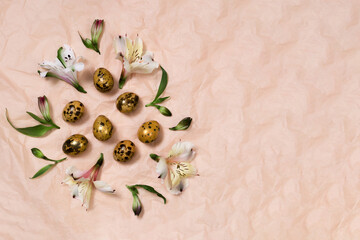 Painted eggs in gold color and spring flowers on a pastel orange background. Spring Easter holiday concept. Place for your text.