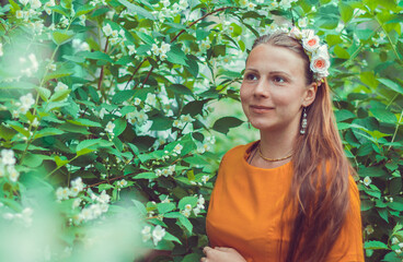 Smiling pretty young woman with long light brown hair wearing a decorative floral headband is looking down away. Portrait of a natural girl without makeup is enjoying the smell in blooming garden.