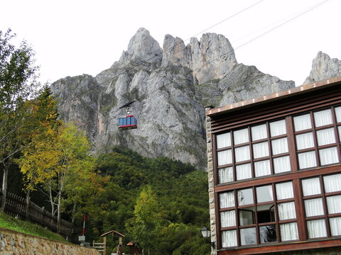 La cabina de un teleférico  asciende hacia la alta montaña enmarcada por los árboles y las edificaciones de la parte baja