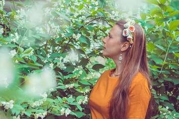 Smiling pretty young woman with long light brown hair wearing a decorative floral headband is looking down away. Portrait of a natural girl without makeup is enjoying the smell in blooming garden.