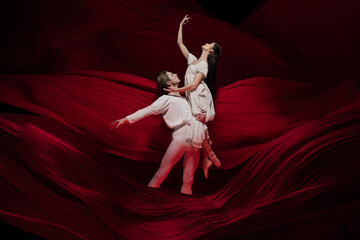 Wine. Young and graceful ballet dancers on red cloth background in classic action. Art, motion,...