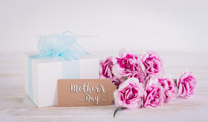 Happy Mother's Day concept. Gift box with flowers and greeting card on white wooden background.