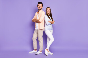 Obraz premium Full size portrait of two cheerful persons standing back to back folded arms isolated on purple color background