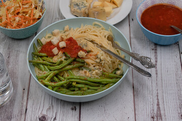 Italian vegetarian angel hair pasta bowl with green beans, red sauce, blue cheese and side salad on wooden background