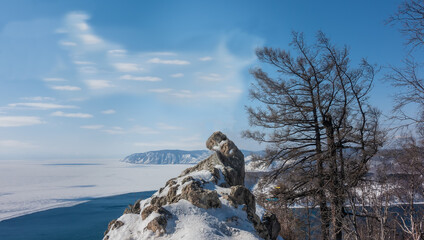 A picturesque stone of a bizarre shape is covered with patches of snow. In the distance you can see a mountain range, the Angara River, the ice of Lake Baikal. Bare branches of trees against the sky.