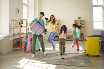 Rest on holidays preparation. Happy family dancing with travel stuff and luggage bag at home living room ready for summer vacation on resort. Overjoyed father, mother and funny daughters travelers