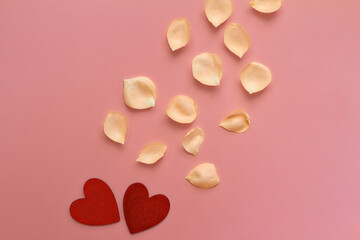 two wooden red heart with flower petals on pink background