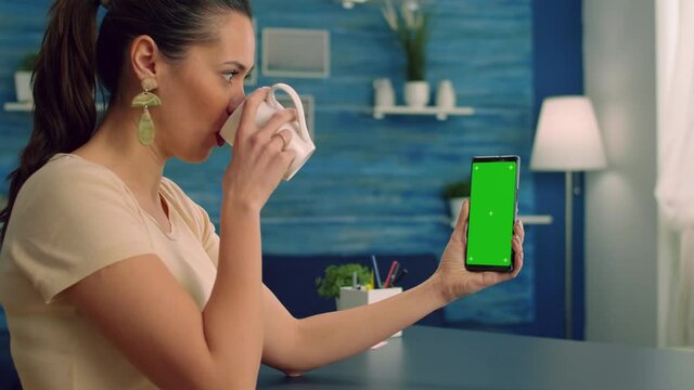 Freelancer using mock up green screen chroma key mobile during online videocall talking with her teamates about online app project standing on office desk. Business woman using isolated technology