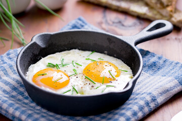 fried eggs with chives in an iron pan on a wooden table
