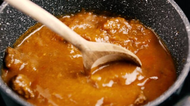 cooking beef goulash mixing with a wooden spoon.Induction cooking beef goulash in a pot for induction.4K Video motion.