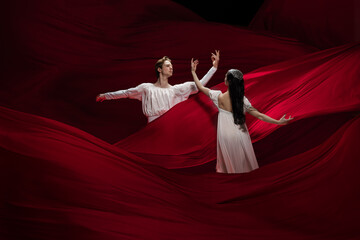 Light. Young and graceful ballet dancers on red cloth background in classic action. Art, motion, action, flexibility, inspiration concept. Flexible caucasian couple with billowing red waves.