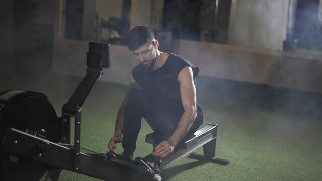 Handsome athlete works out in gym with rowing machine