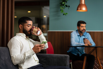 business man checking report on smart phone and drinking coffee on sofa in office lobby. .