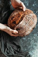 Male hands hold homemade bread on dark background. Bread with nuts and candied fruits.