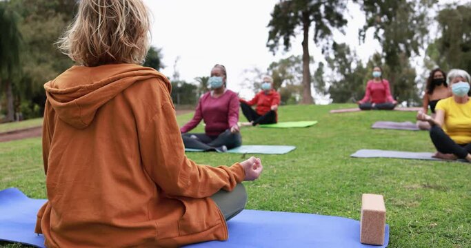 People doing yoga class outdoor sitting on grass while wearing safesty masks during coronavirus outbreak - Social distance and sport concept 