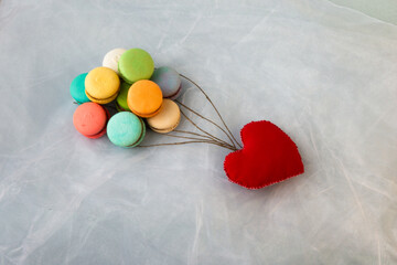 Multicolored macarons like balls and a red heart on a gray background.