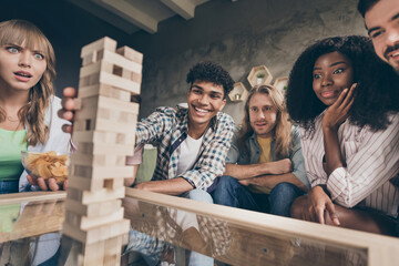 Portrait of attractive cheerful friends gathering playing brick game pastime in house loft brick...