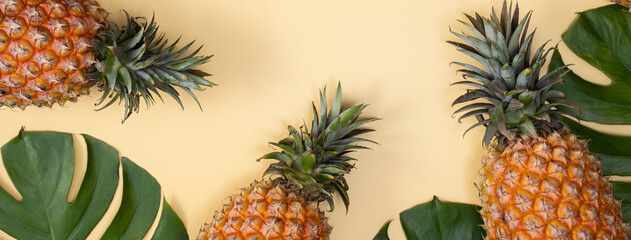 Fototapeta premium Top view of fresh pineapple with tropical leaves on yellow background.