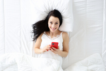 Young woman lying in bed with phone top view