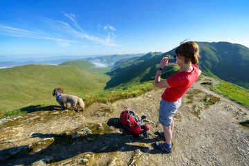 A female hiker taking photos down the glen of Allt a Chobhair from the mountain summit of Beinn Ghlas in the Scottish Highlands, UK landscape.