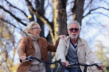 Cheerful active senior couple with bicycle in public park together having fun. Perfect activities for elderly people. Happy mature couple riding bicycles in park