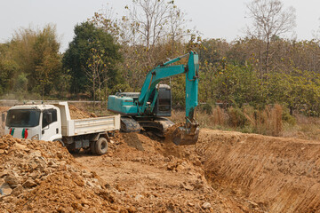 Cyan excavator digging the soil into a truck ,In the construction site area