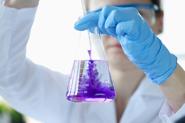 Woman scientist dripping purple liquid into flask with solvent closeup