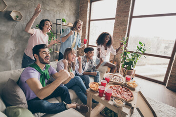 Portrait of attractive cheerful friends sitting on sofa having fun watching film movie cinema in house loft style interior indoors