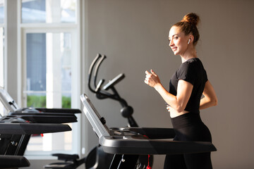 young sports woman working out and running on treadmill in gym