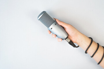 Male hand holding studio microphone, top view, light background. Cable is wrapped around the arm....