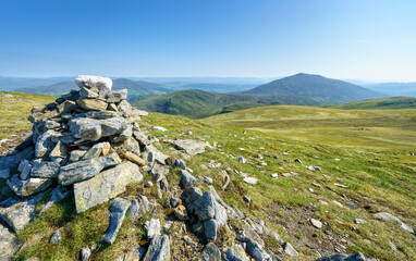 A pile of stones marking the mountain top of Meall a Bharr with the summit of Schiehallion in the distance in the Scottish Highlands, UK landscapes.