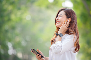 Beautiful smiling Asian woman walking and using a smartphone on the street on a sunny summer day in the park.