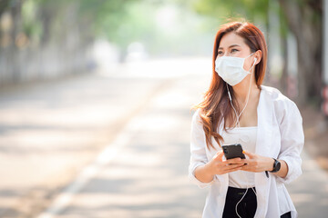 Young asian women Wearing a mask to prevent COVID-19 is using a smartphone on the street on a sunny...