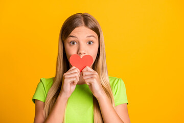 Photo of young preteen girl cover mouth red paper heart excited valentine day isolated over yellow color background