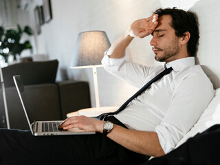 Young businessman rests after a long day. Man working on laptop in the bed.