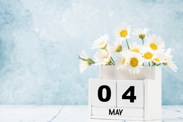 cube calendar for May decorated with daisy flowers over blue with copy space