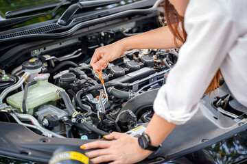 Beautiful woman checking car engine oil By pulling the dipstick to see the oil level of their own car.