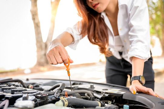 Beautiful woman checking car engine oil By pulling the dipstick to see the oil level of their own car.