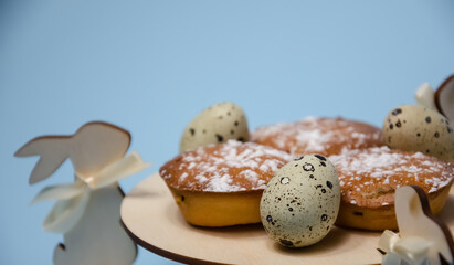 Happy Easter decoration: Selective focus muffins and quail eggs on wooden stand with Easter bunnies on blue background with copy space. Preparation for the holiday. Easter holiday banner.