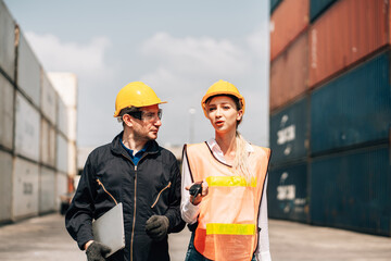 workers teamwork man and woman in safety jumpsuit workwear with yellow helmet use laptop and talking at cargo container shipping warehouse. transportation import,export logistic industrial service