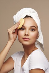 Nice girl with a soft sponge in hand and a towel on her head