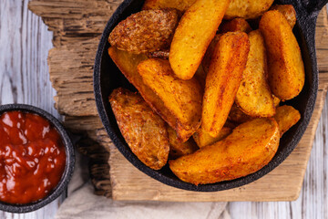 Fried potatoes on a black frying pan. Portion of fresh baked potato.